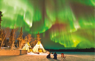 Aurora Village in Yellowknife, Canada is a popular destination to see the Northern Lights up close  The camp s glowing teepees complement the colorful ribbon of lights above 